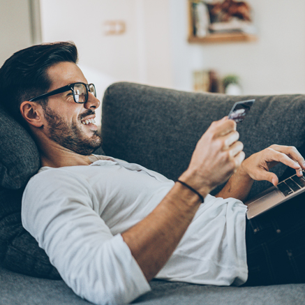 Man laying on couch with laptop and debit card typing